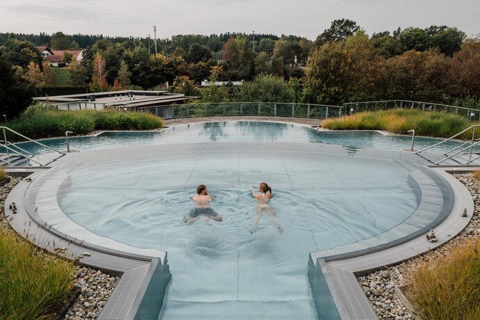 Paar schwimmt im Kaskaden-Becken des Spa Resort Geinberg mit Blick auf die Innviertler Umgebung | © Spa Resort Geinberg / Chris Perkles