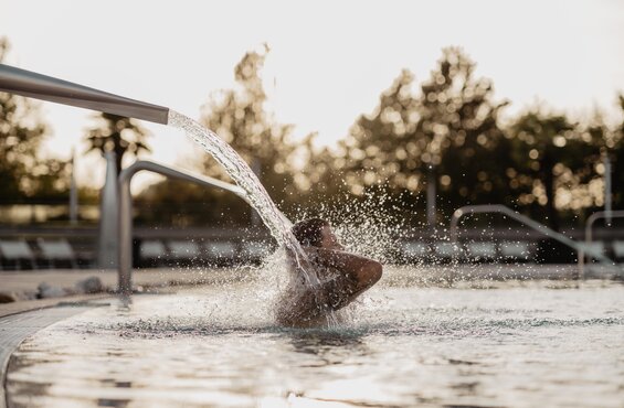 Mann genießt das Wasser der Schwalldusche im Thermal-Becken outdoor im Spa Resort Geinberg | © Spa Resort Geinberg / Chris Perkles